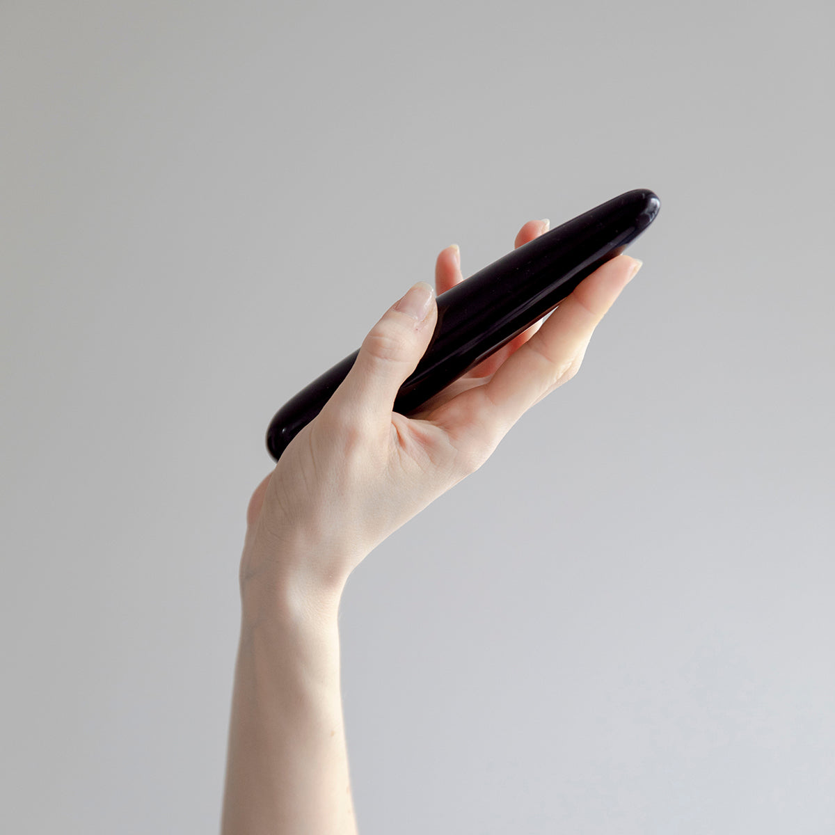 Hand holding the Chakrubs Xaga Slim Non-Phallic Dildo against a minimalist background.