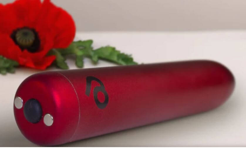 Poppy Red Rechargeable Bullet Vibrator resting near a red poppy flower against a light background.