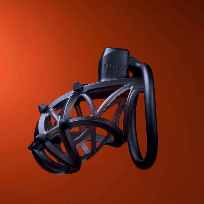 UPKO Caged Beast Male Chastity Device Kit in sleek black against a textured orange background, showcasing unique design and comfort.