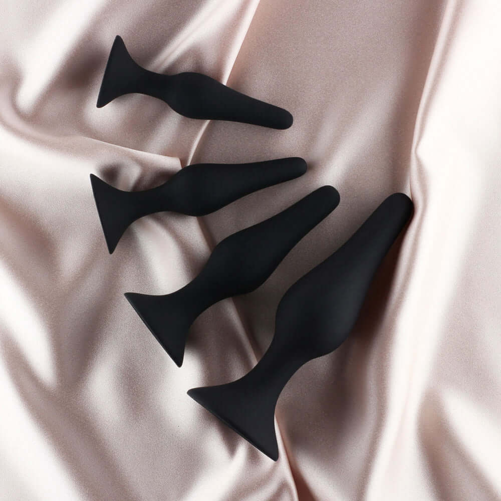 Edonista Alessandra 4 Piece Silicone Anal Plug Set Black displayed on soft satin fabric.