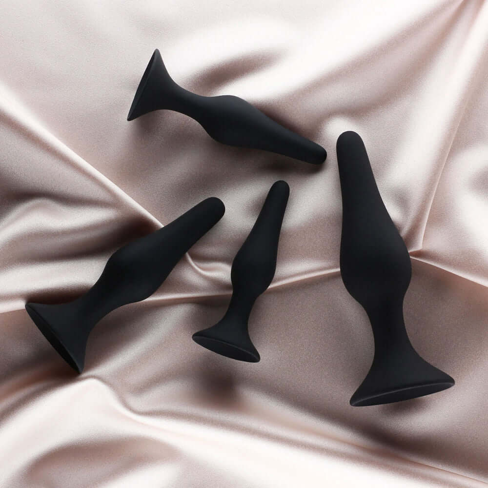 Edonista Alessandra 4 Piece Silicone Anal Plug Set Black displayed on a satin surface, featuring various sizes for comfortable use.
