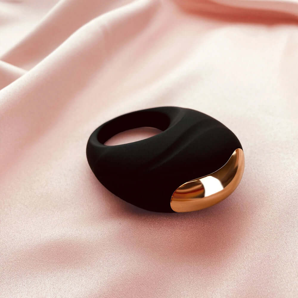 Edonista Luca Vibrating Penis Ring Black on soft pink fabric, featuring sleek design and gold accents.