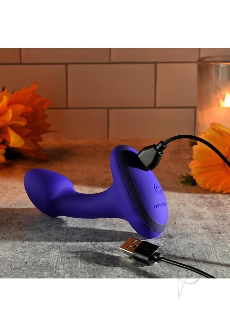 Gender X Anybody's Plug Silicone Vibrating Butt Plug Blue charging with a USB cable on a textured surface.