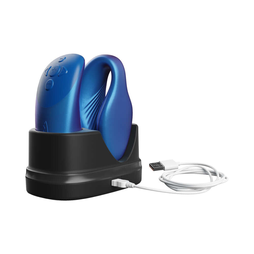 We-Vibe Chorus Couples Massager Cosmic Blue charging on a sleek black dock with USB cable.