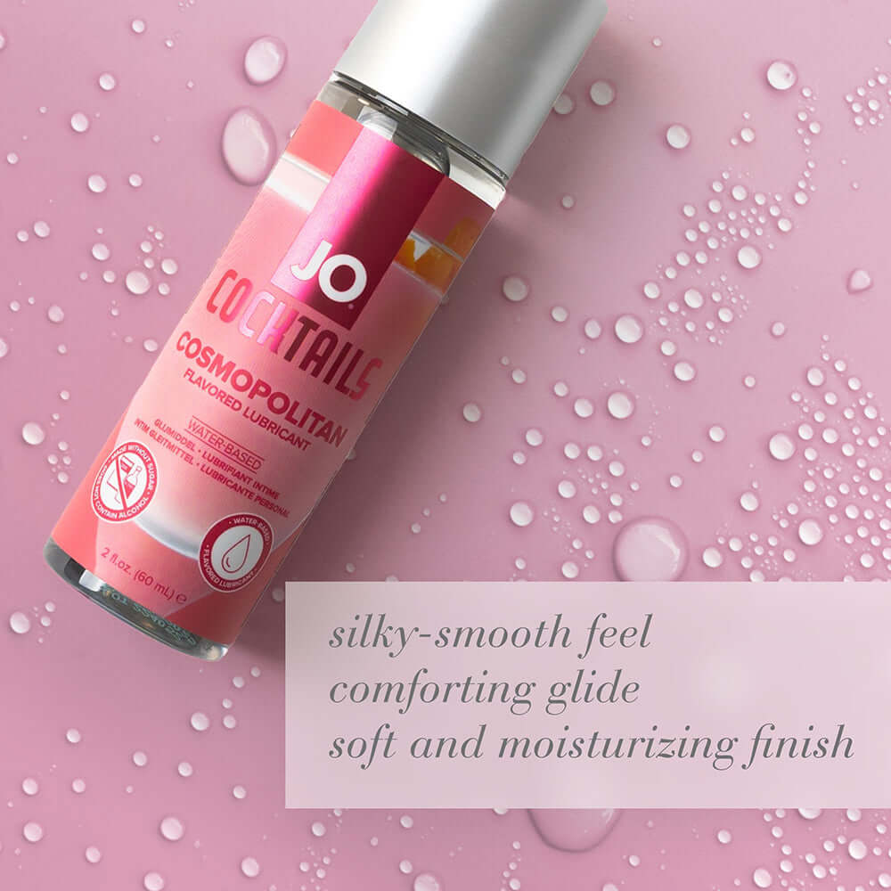 JO Cocktails Cosmopolitan Flavored Water-Based Lubricant 2 Oz bottle on a pink background with water droplets.