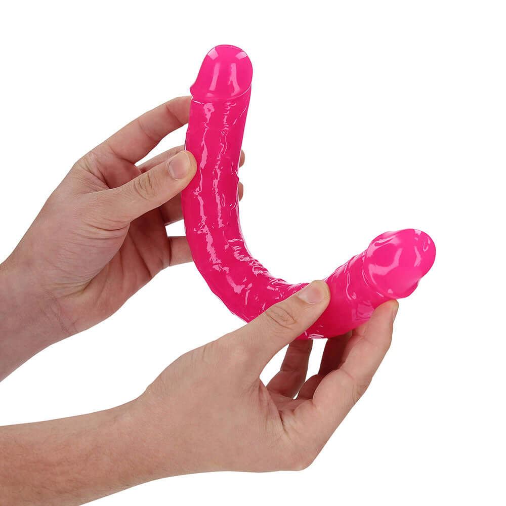 RealRock Glow in the Dark Double Dong 12 inch Neon Pink held in hands, showcasing its flexible and vibrant design.
