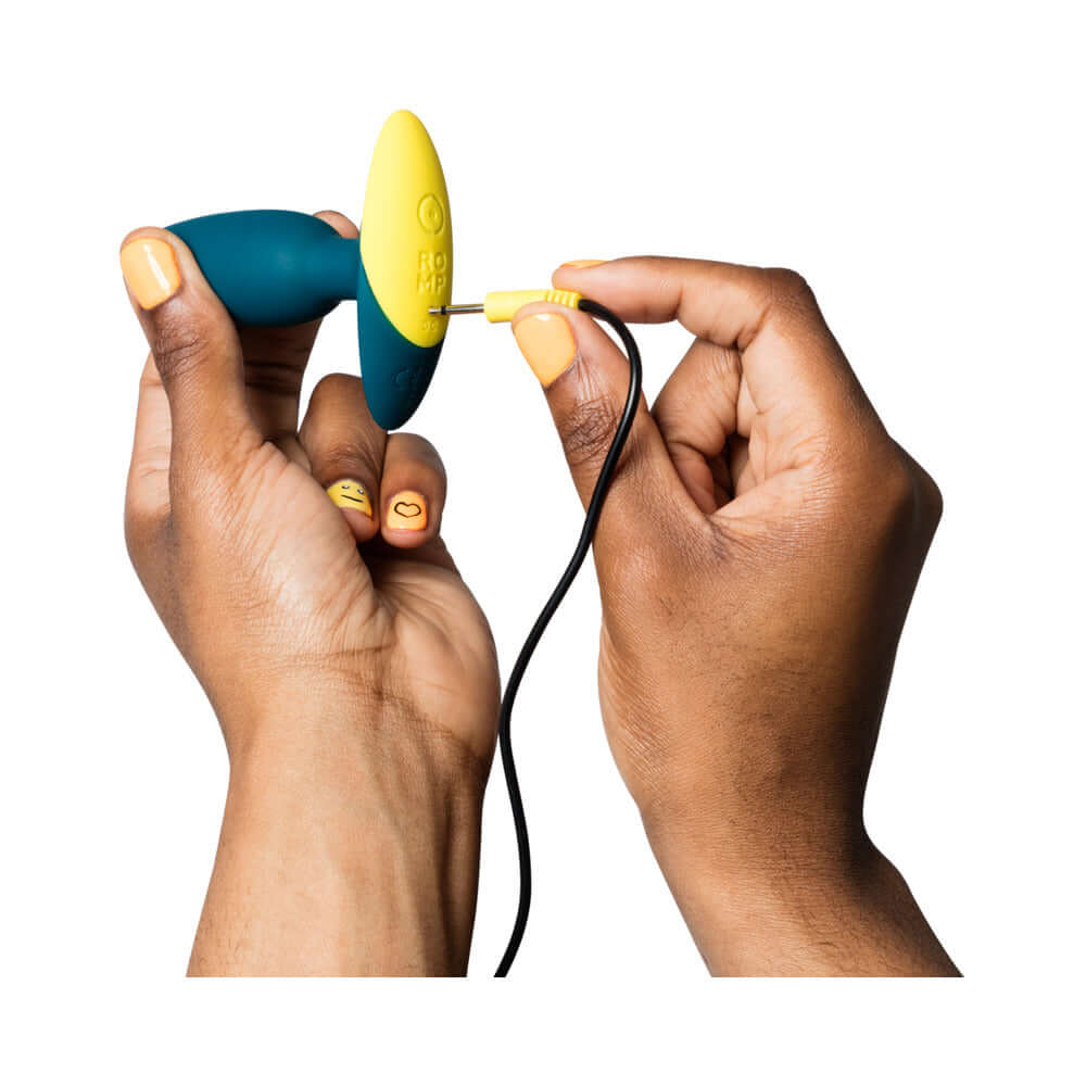 Person holding the ROMP Bass Rechargeable Silicone Vibrating Anal Plug Dark Green while connecting it for charging.