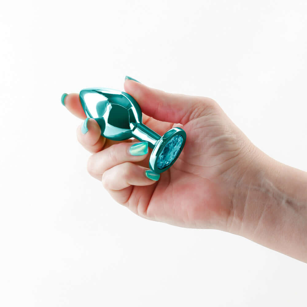Rear Assets Metal Anal Plug Medium Teal held in hand, showcasing its chrome-plated aluminum design and striking teal finish.