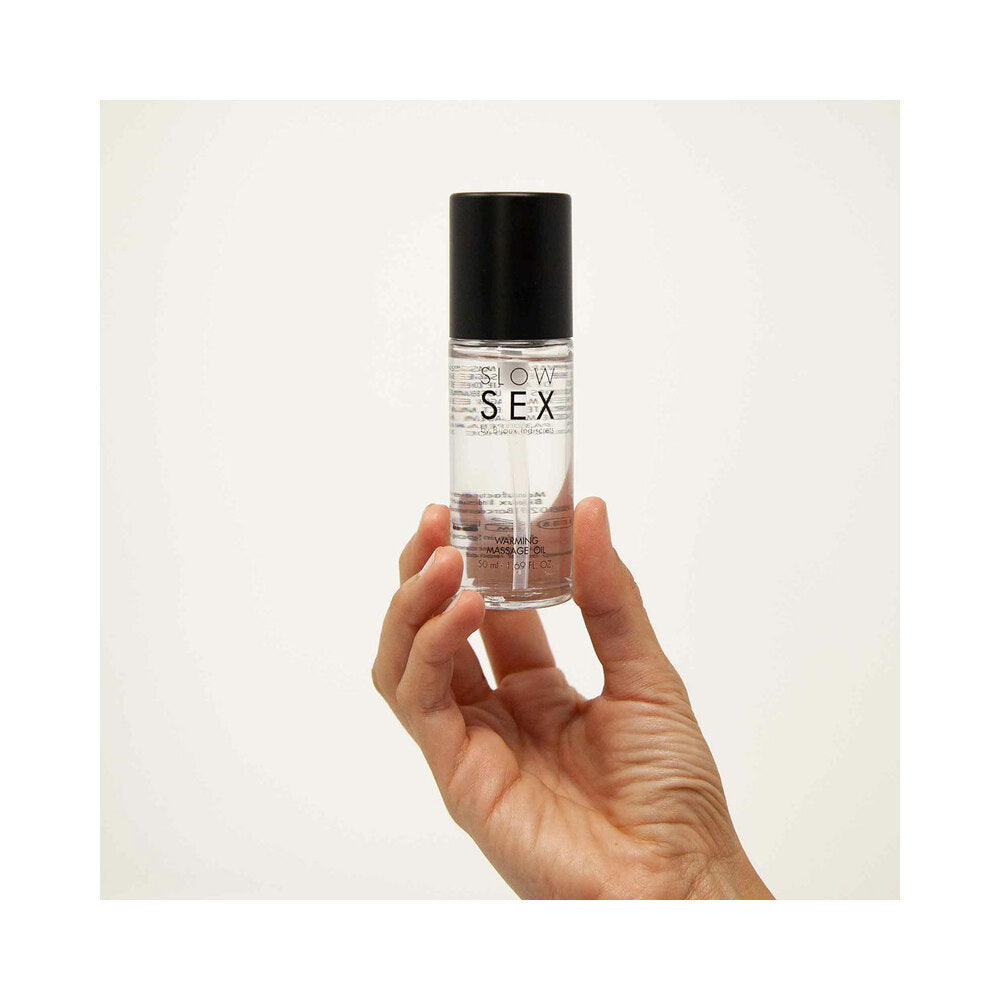 Bijoux Indiscrets Slow Sex Warming Massage Oil 1.69 Oz held in hand with a soft focus background.