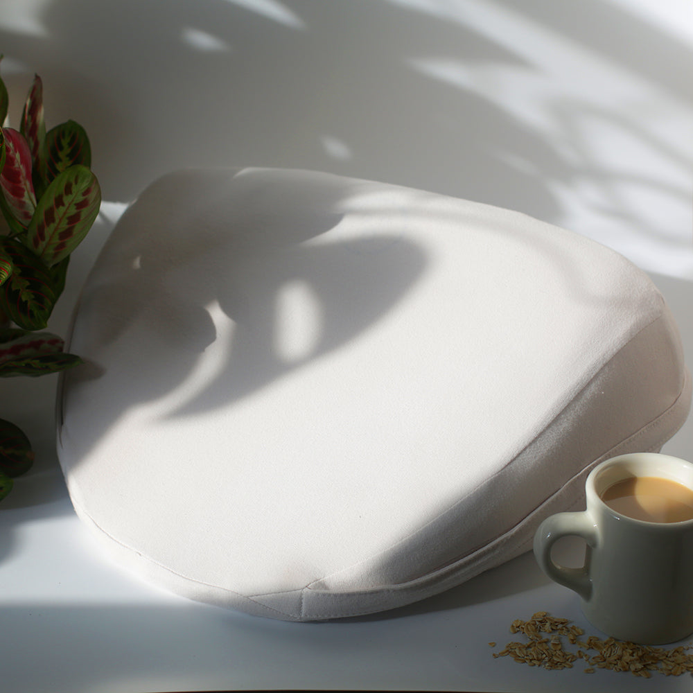Dame Pillo Sex Pillow Oat on a surface with a cup of coffee in the background, designed for intimate comfort.