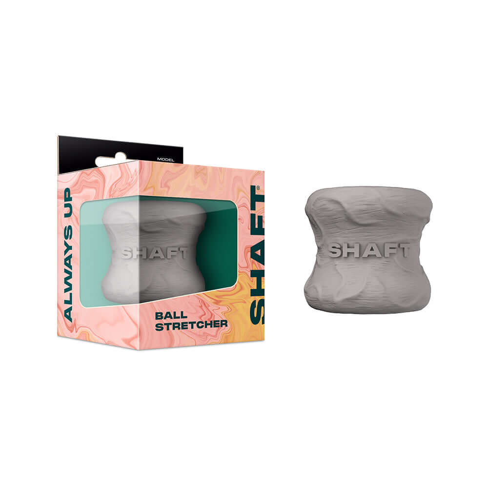 Shaft Model H Ballstretcher Gray next to its packaging, showcasing a flexible body-safe design for intimate play.