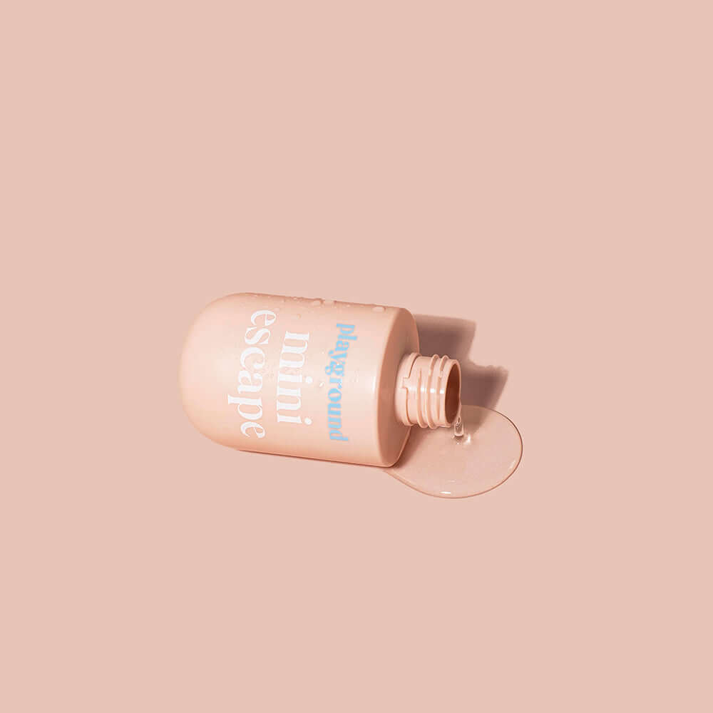 Playground Mini Escape Water-Based Personal Lubricant 3.7 Oz bottle with lubricant oozing out, placed on a soft pink background.