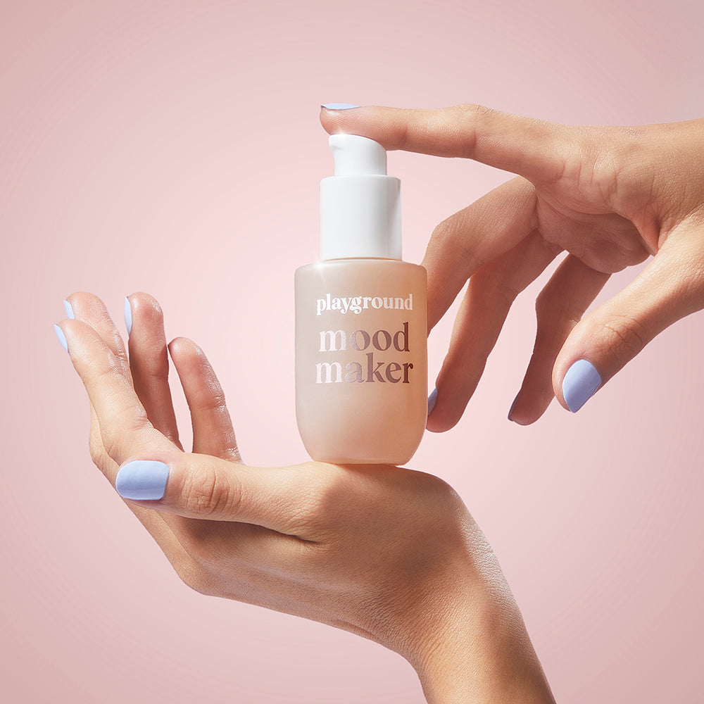 Playground Mood Maker Intimacy Oil 30 ml bottle held in hands on a pink background.