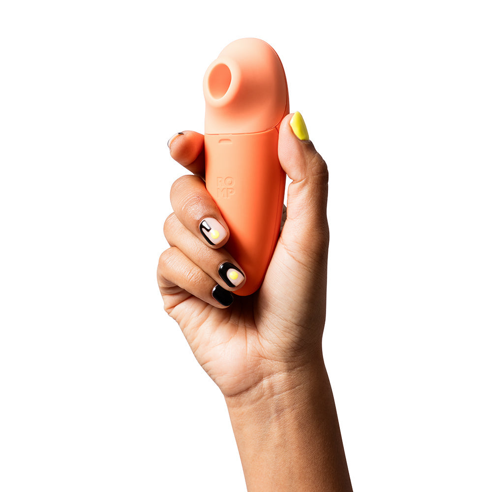Hand holding the ROMP Switch X Clitoral Stimulator in a vibrant orange color.