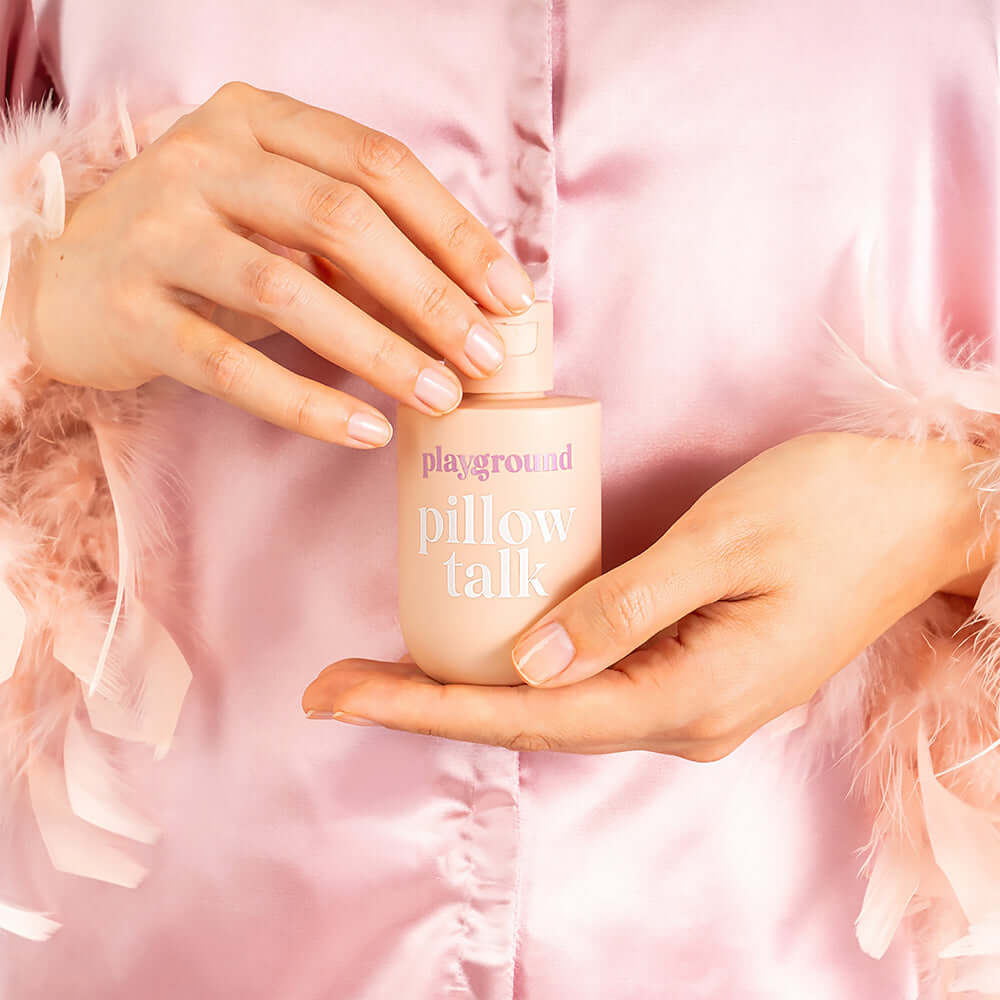Playground Pillow Talk Water-Based Personal Lubricant bottle held by a person in a silky robe.
