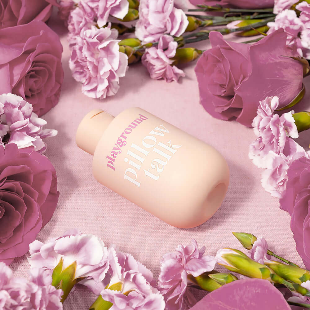 Playground Pillow Talk Water-Based Personal Lubricant bottle surrounded by pink roses and flowers.