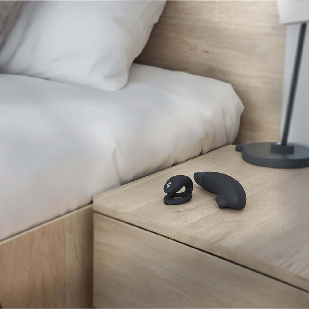 Womanizer x We-Vibe Lust and Luxury Collection Black devices on a nightstand beside a bed.