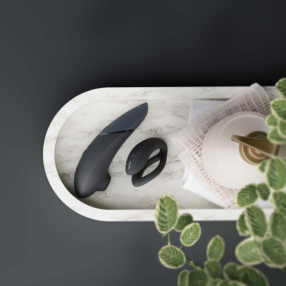 Womanizer x We-Vibe Lust and Luxury Collection Black on tray with plants, offering sophistication and intimate innovation.