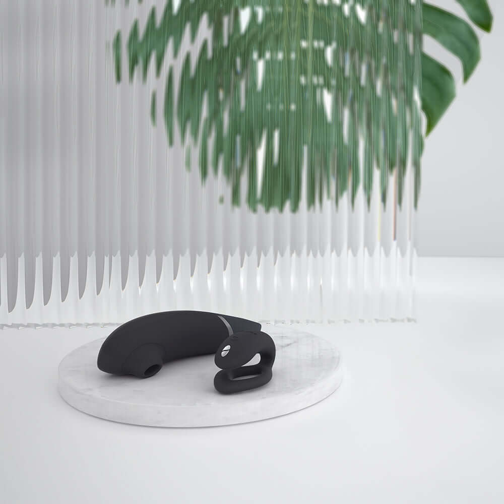 Womanizer x We-Vibe Lust and Luxury Collection Black on a marble surface with greenery in the background.