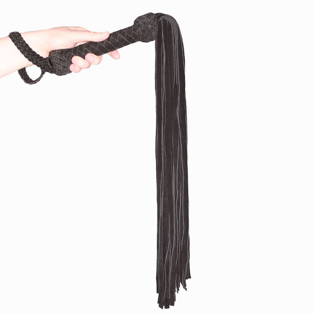 Prowler Red Leather Suede Flogger Black in hand, featuring a suede-wrapped handle and long tasseled strands.
