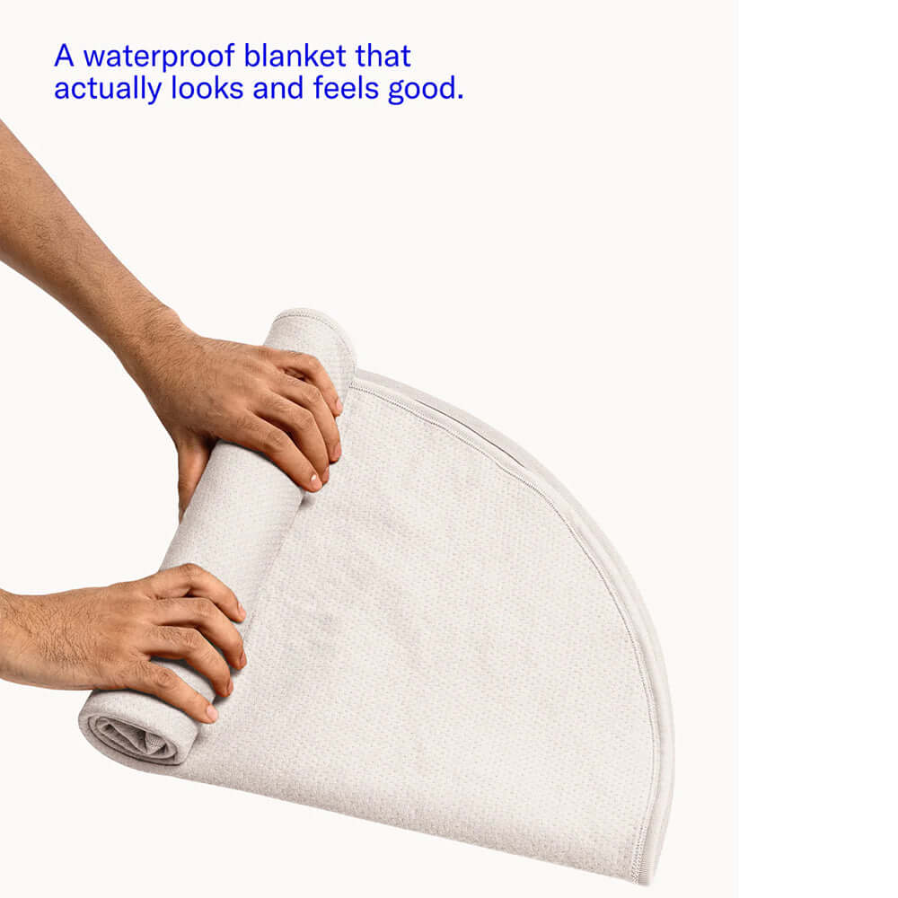 Person rolling up the Dame Thro Waterproof Sex Blanket Oat showcasing its waterproof feature.