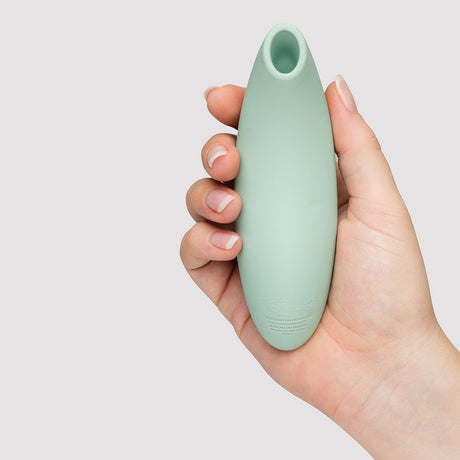We-Vibe Melt 2 Pleasure Air Clitoral Stimulator Sage held in a hand against a neutral background.