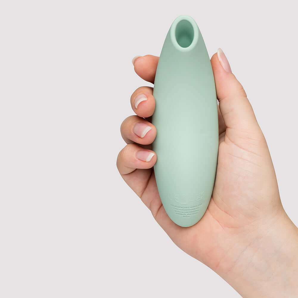 We-Vibe Melt 2 Pleasure Air Clitoral Stimulator Sage held in a hand against a neutral background.