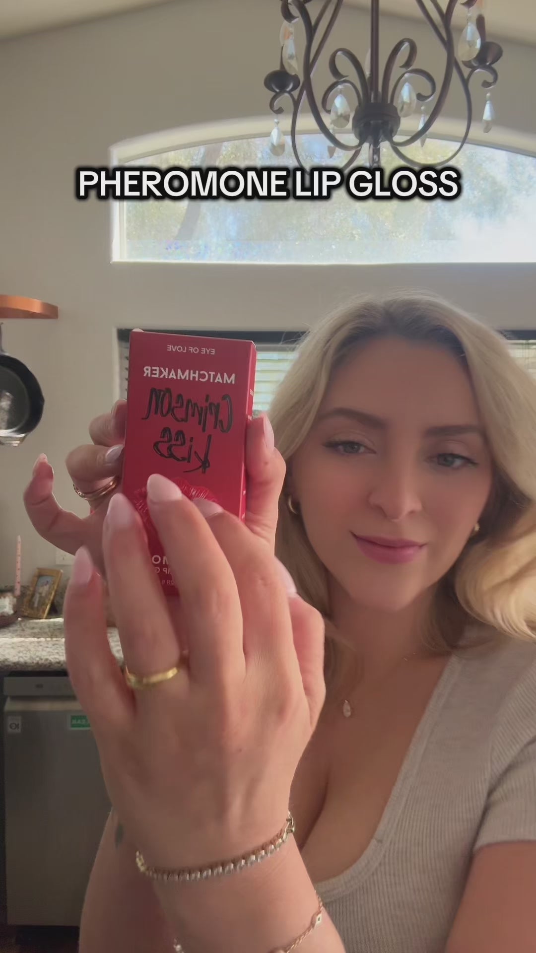 Close-up of Eye Of Love Matchmaker Pheromone Plumping Lip Gloss Crimson Kiss in a woman's hand.
