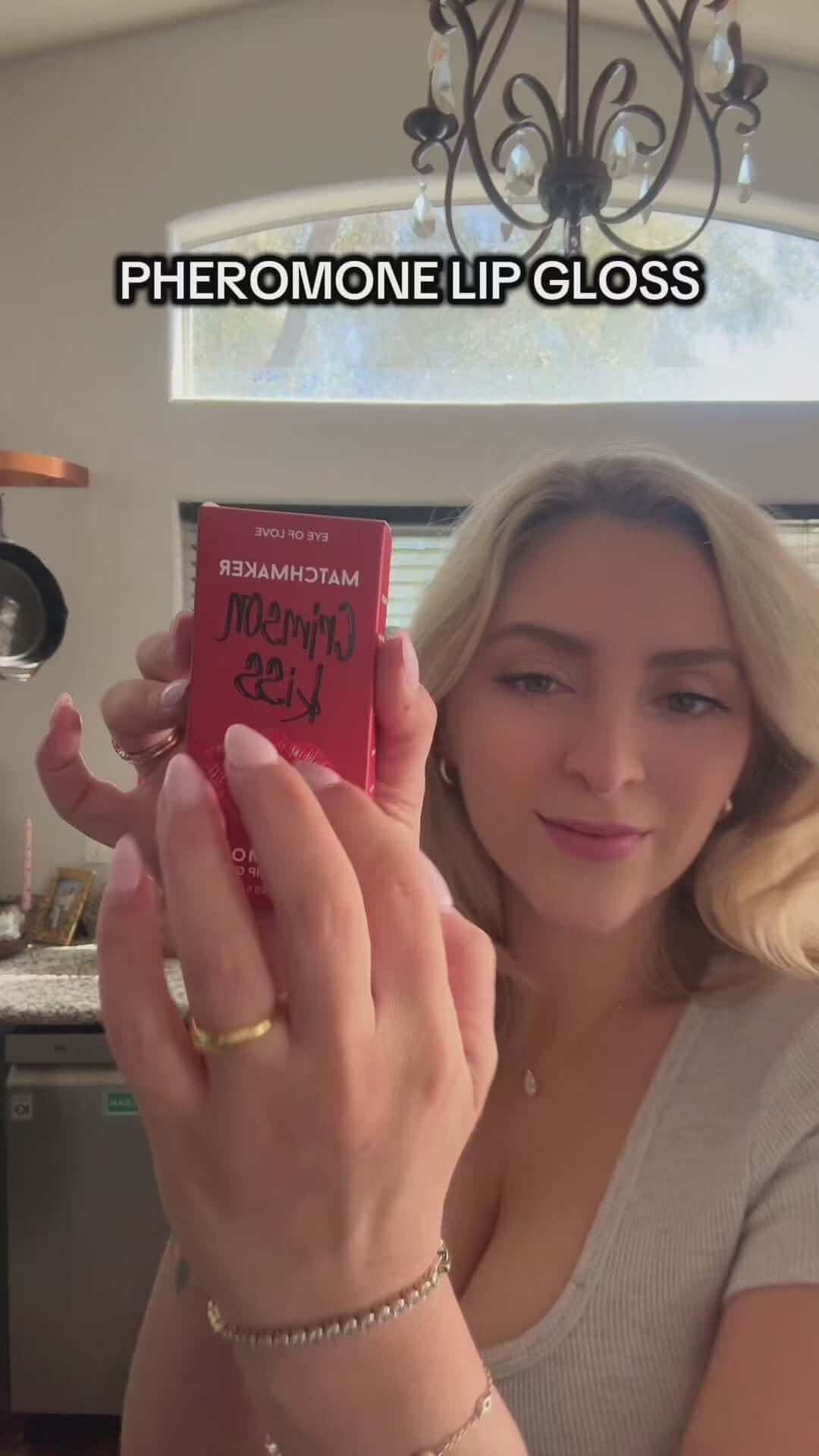 Close-up of Eye Of Love Matchmaker Pheromone Plumping Lip Gloss Crimson Kiss in a woman's hand.