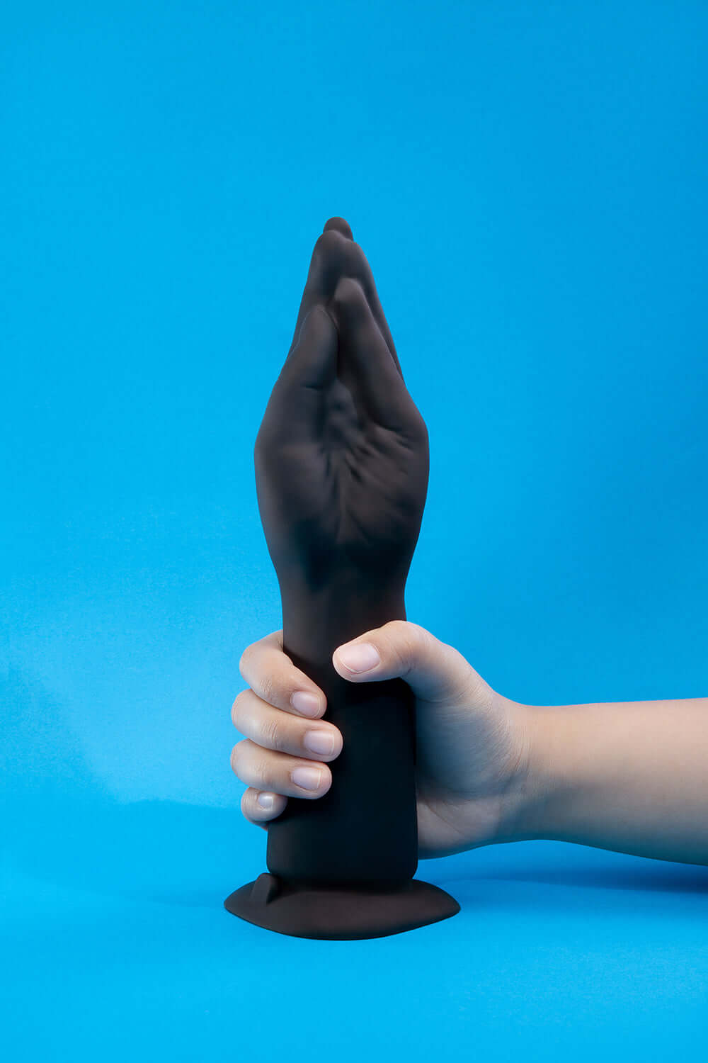 b-Vibe Vibrating Silicone Fisting Dildo held by a hand against a solid blue background.