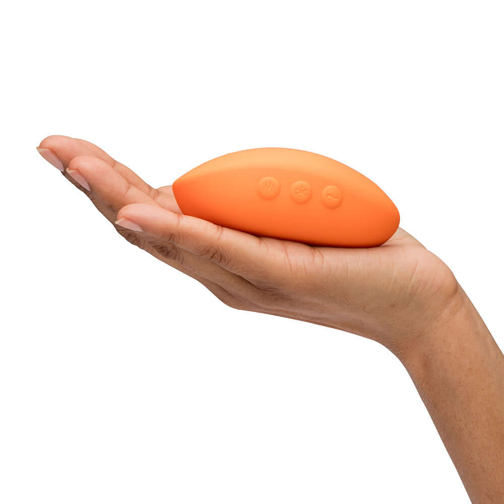 We-Vibe Temp Clitoral Massager Tangerine held in a hand, showcasing its ergonomic design and vibrant color.