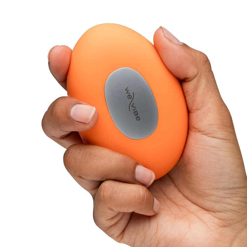 We-Vibe Temp Clitoral Massager Tangerine held in hand showcasing ergonomic design and vibrant color.