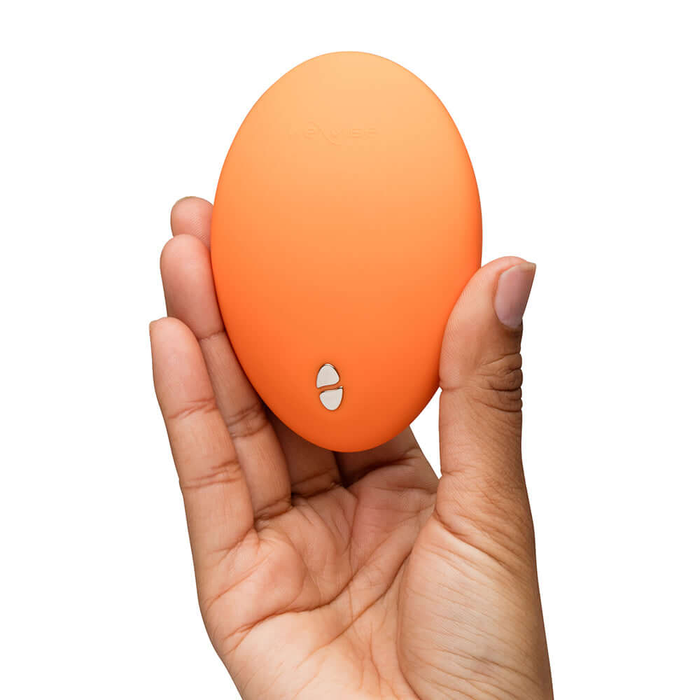 We-Vibe Temp Clitoral Massager Tangerine held in hand, featuring ergonomic design and sleek orange exterior.