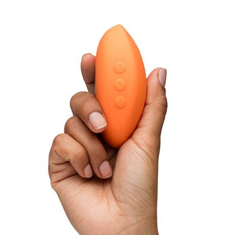We-Vibe Temp Clitoral Massager Tangerine held in hand, showcasing its ergonomic design and vibrant color.