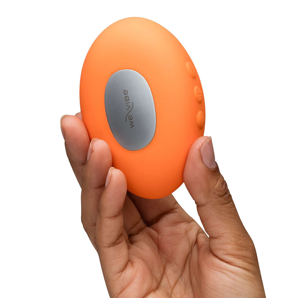 We-Vibe Temp Clitoral Massager Tangerine held in hand showcasing its ergonomic design and vibrant color.