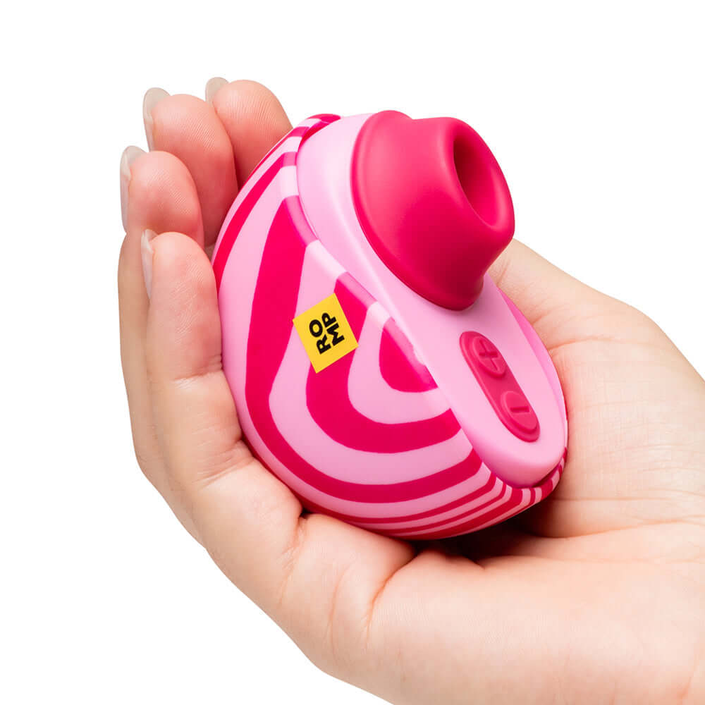 ROMP Spin Travel Rechargeable Clitoral Stimulator held in a hand with a pink and white design.