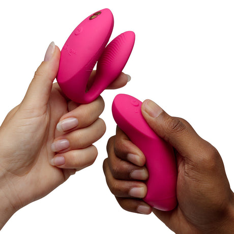 We-Vibe Chorus Pro Couples Massager Electric Pink held by two individuals with different skin tones.