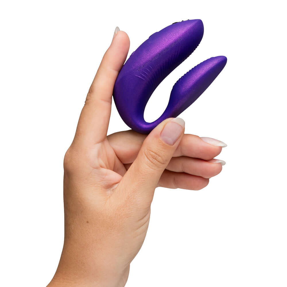 Hand holding the We-Vibe Chorus Pro Cosmic Purple couples vibrator, showcasing its ergonomic design.