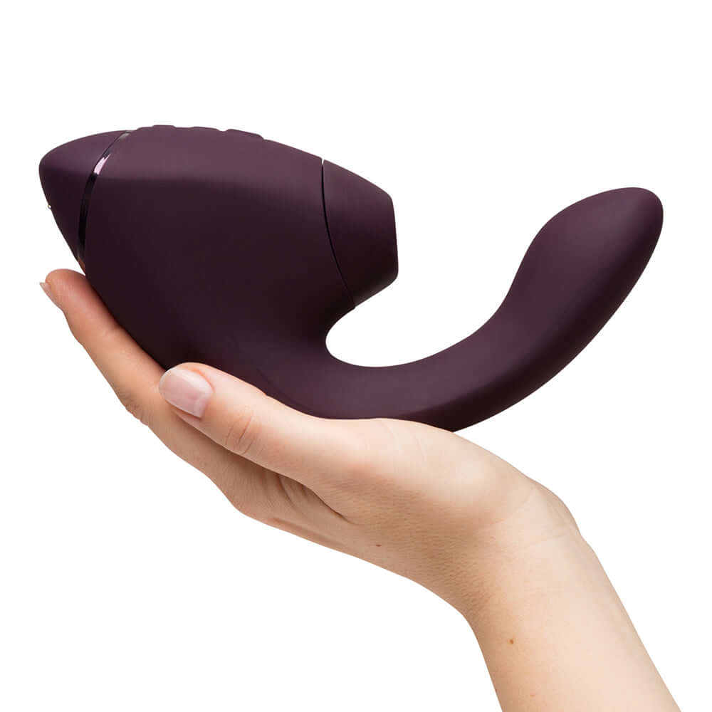 Womanizer Next Duo Massager Dark Purple held in a hand, showcasing its ergonomic design and dual stimulation features.