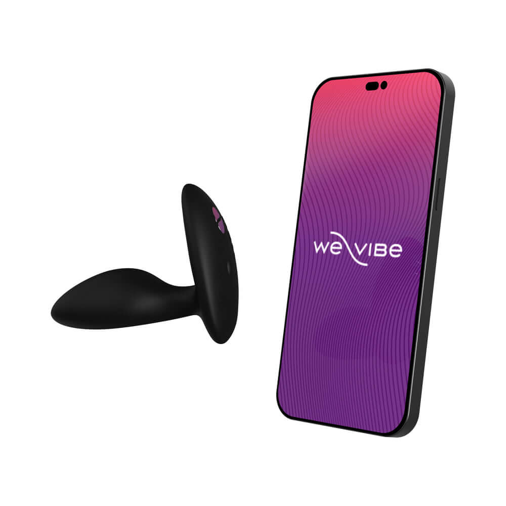 We-Vibe Ditto Plus Remote Control Vibrating Anal Plug Black next to a smartphone displaying the We-Vibe logo.