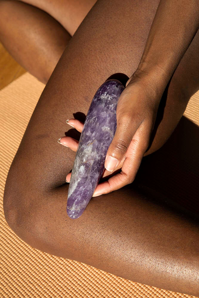 Chakrubs Amethyst Original Wand held by a person, showcasing its luxurious amethyst crystal design on a yoga mat.