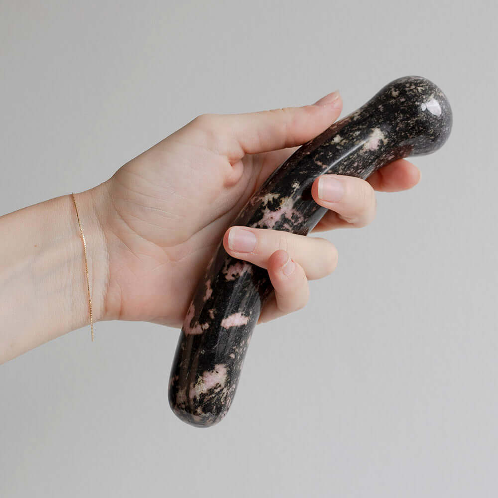Hand holding the Chakrubs Anahata Curve Rhodonite Wand, a crystal pleasure tool for heart opening and emotional balance.