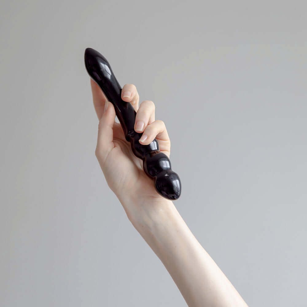 A hand holding the Chakrubs Xaga Viper Obsidian Wand, showcasing its unique curvature and ridged design.