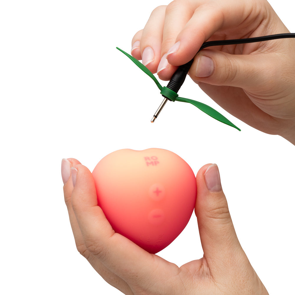 Romp Pink Peach Air Suction Clitoral Stimulator being charged with hand holding it.