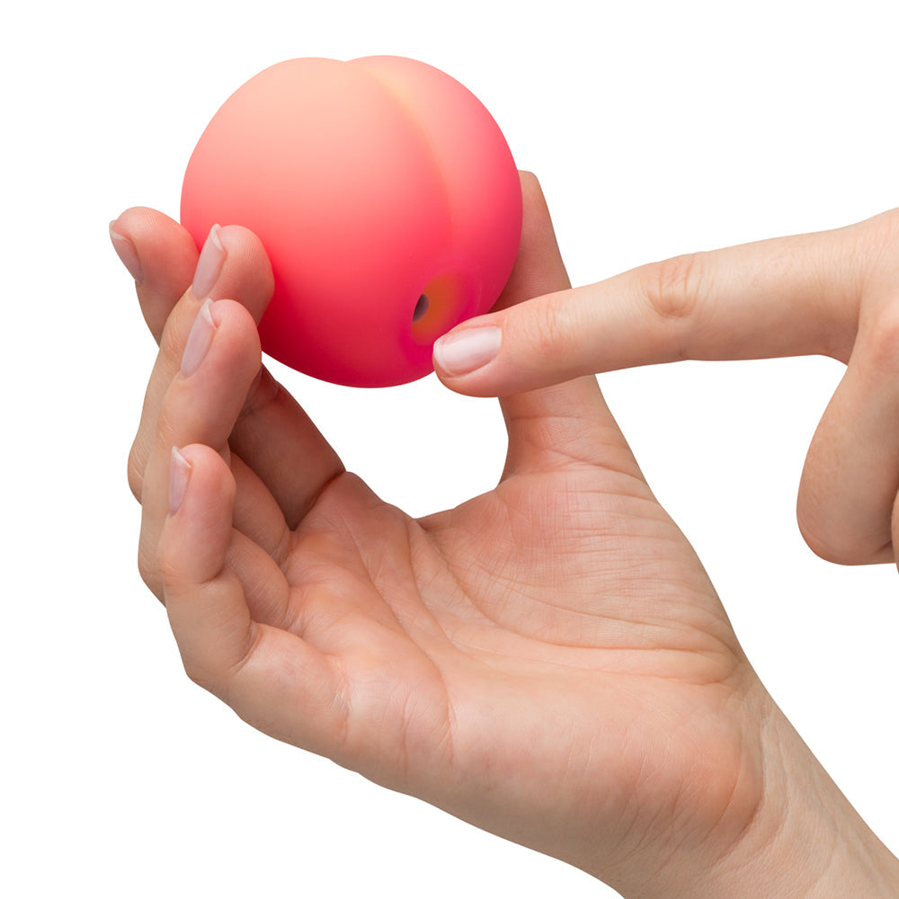 Romp Pink Peach Air Suction Clitoral Stimulator held in hand, showcasing its playful peach-inspired design and soft texture.