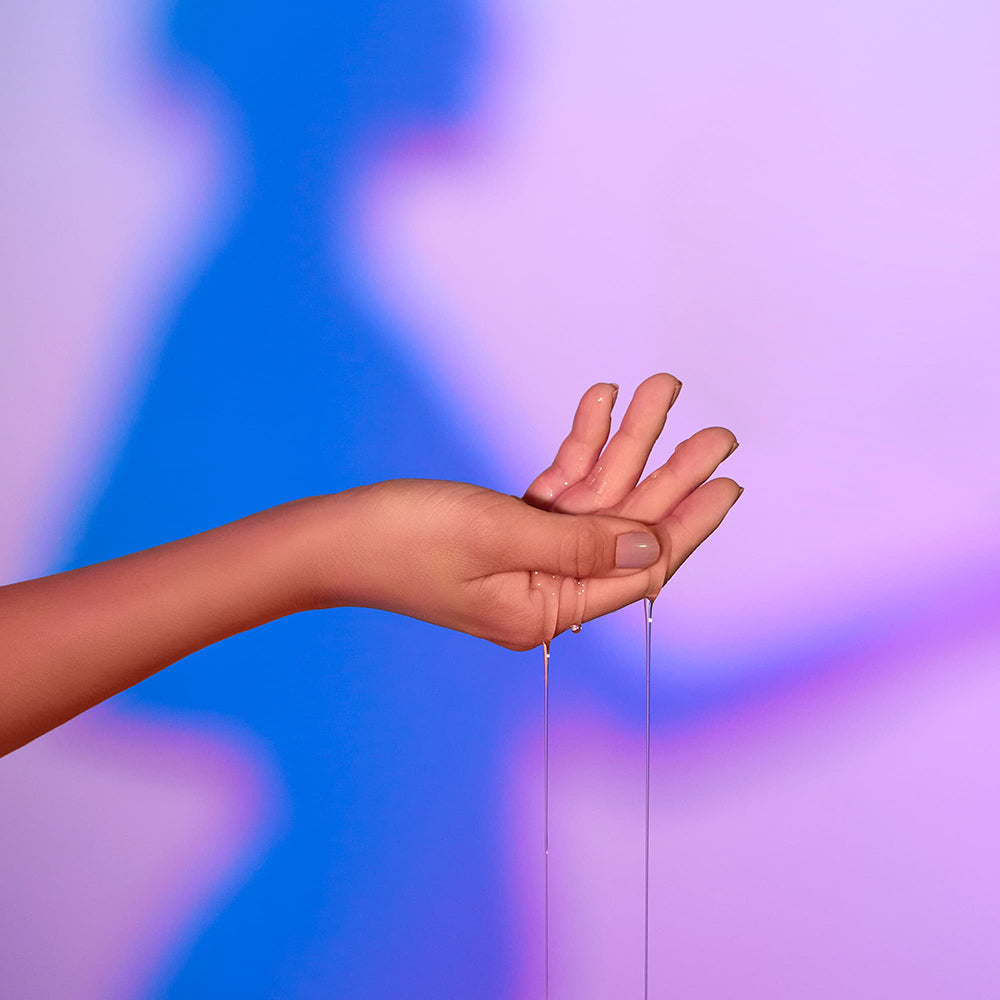 Love Me Tender Strawberry Heating Massage Oil dripping from a hand against a colorful backdrop.