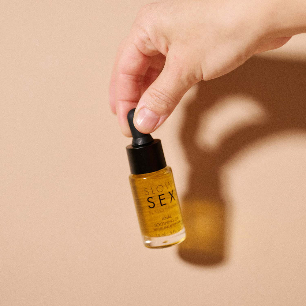 Slow Sex Anal Soothing Oil Before And After Care in a dropper bottle held by a hand.