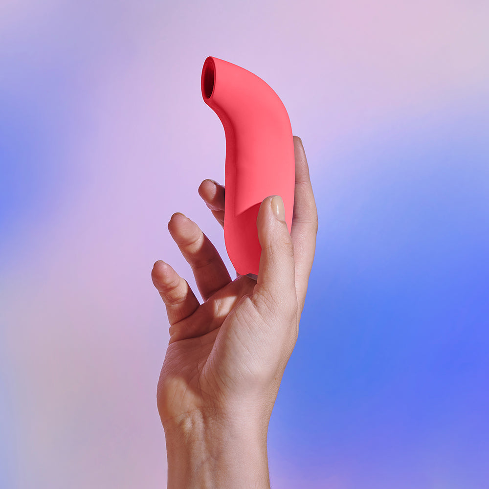 Dame Aer Suction Massager Coral in hand with soft background colors