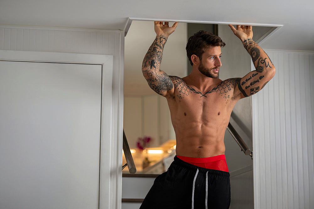 Male Power Mesh 2.0 Mini Short Red XL worn by a tattooed man, showcasing sporty style and comfort in a modern indoor setting.