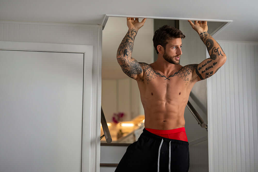 Male Power Mesh 2.0 Mini Short Red XL worn by a tattooed man, showcasing sporty style and comfort in a modern indoor setting.